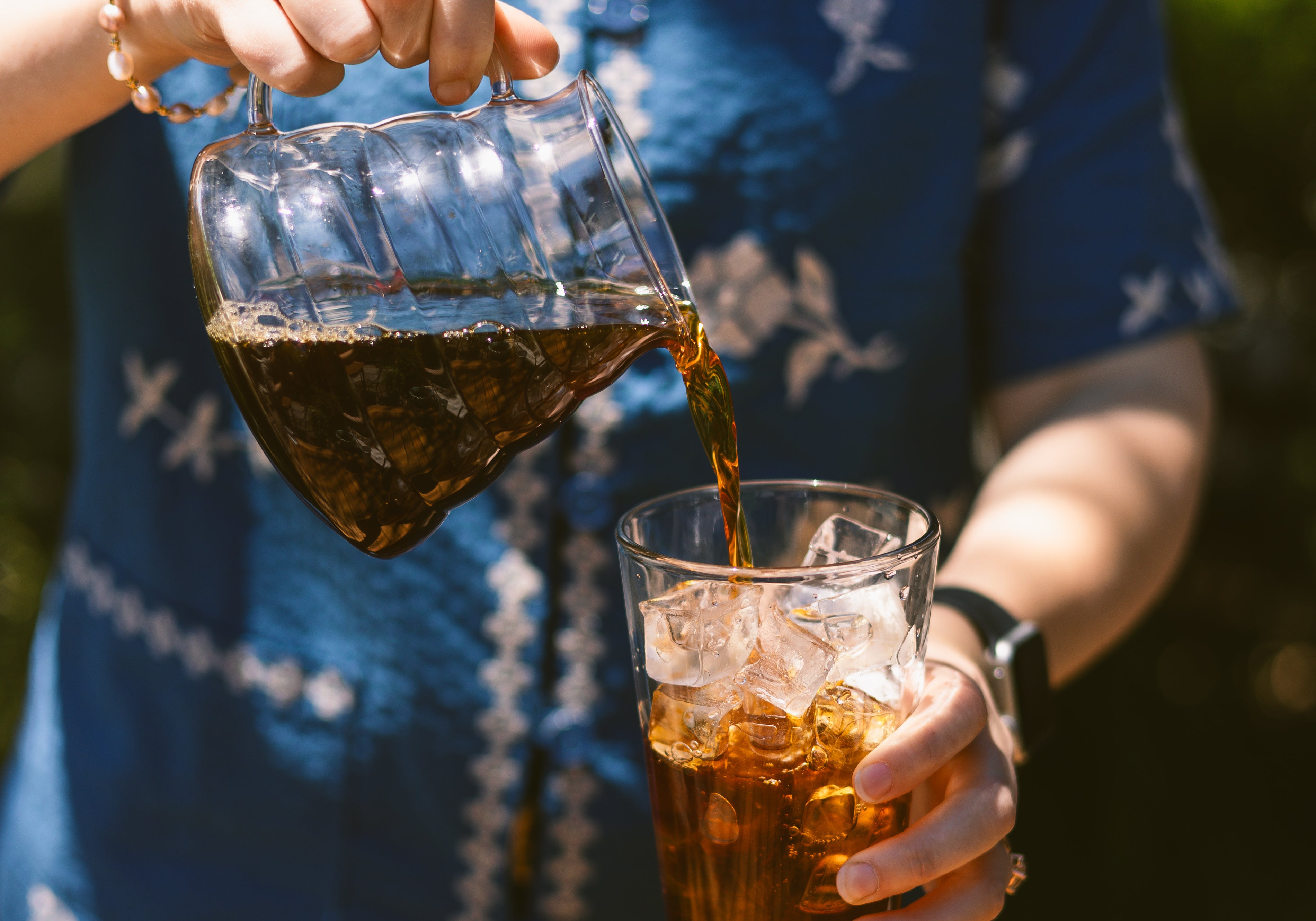 Person pouring coffee from ranger server into a pint glass filled with ice.