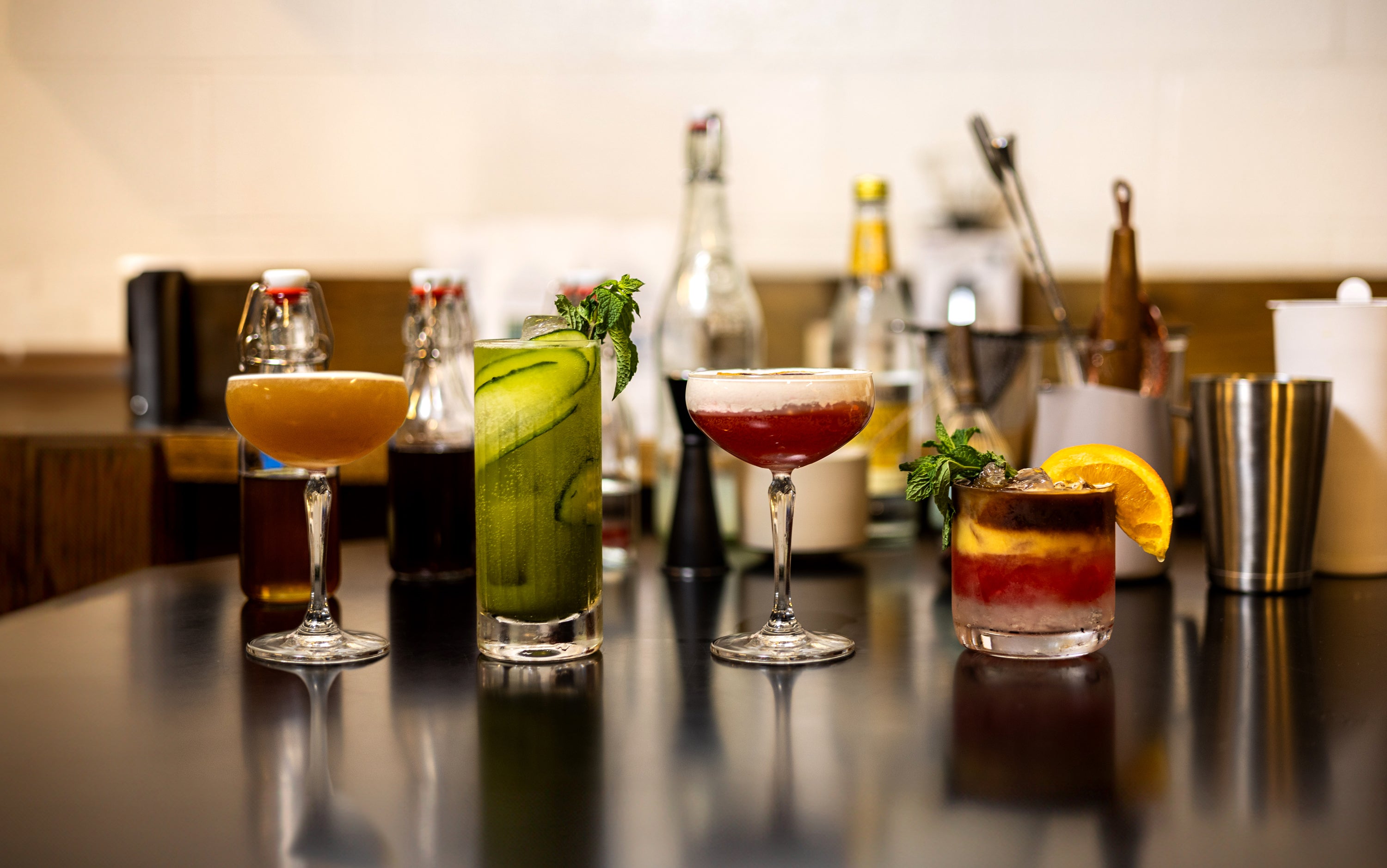 Four drinks on a black table surrounded by bar supplies.