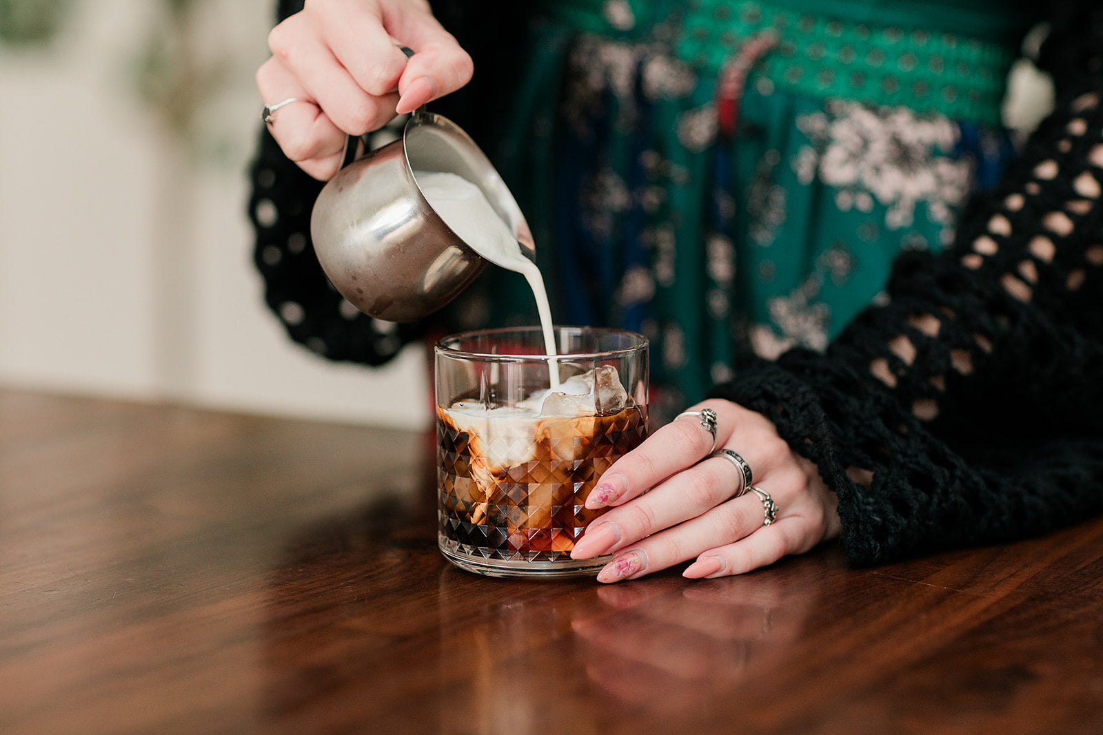 Person pouring milk into an iced coffee beverage in a glass