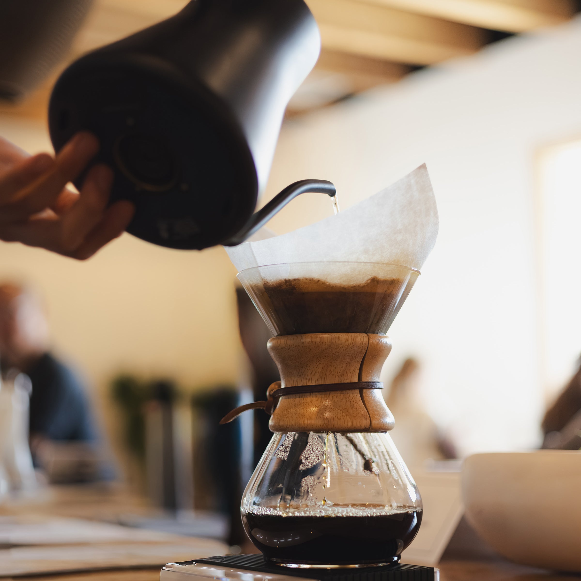 Person pouring coffee into a Chemex filter on a wooden table.