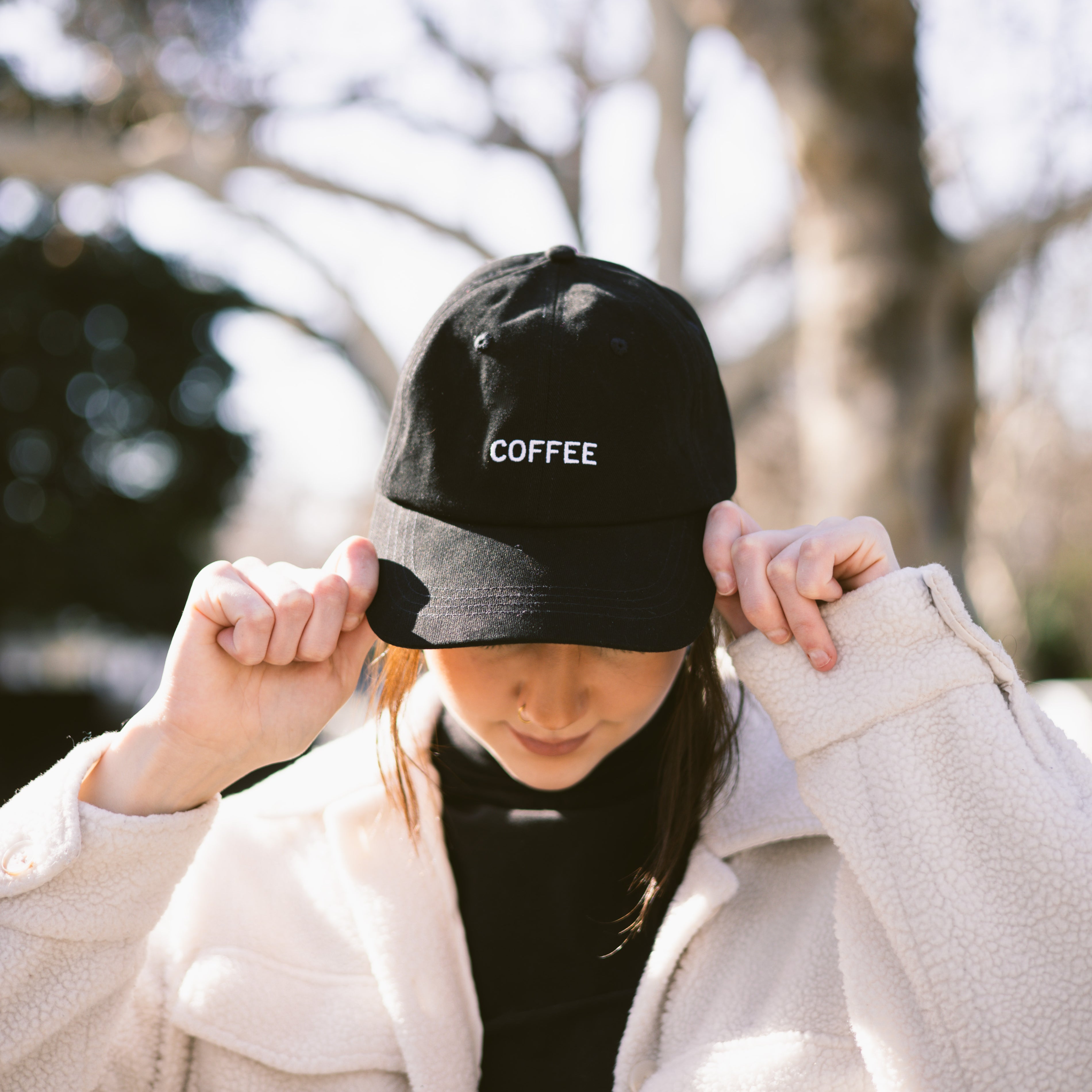 Person wearing a black cap with 'COFFEE' text outdoors