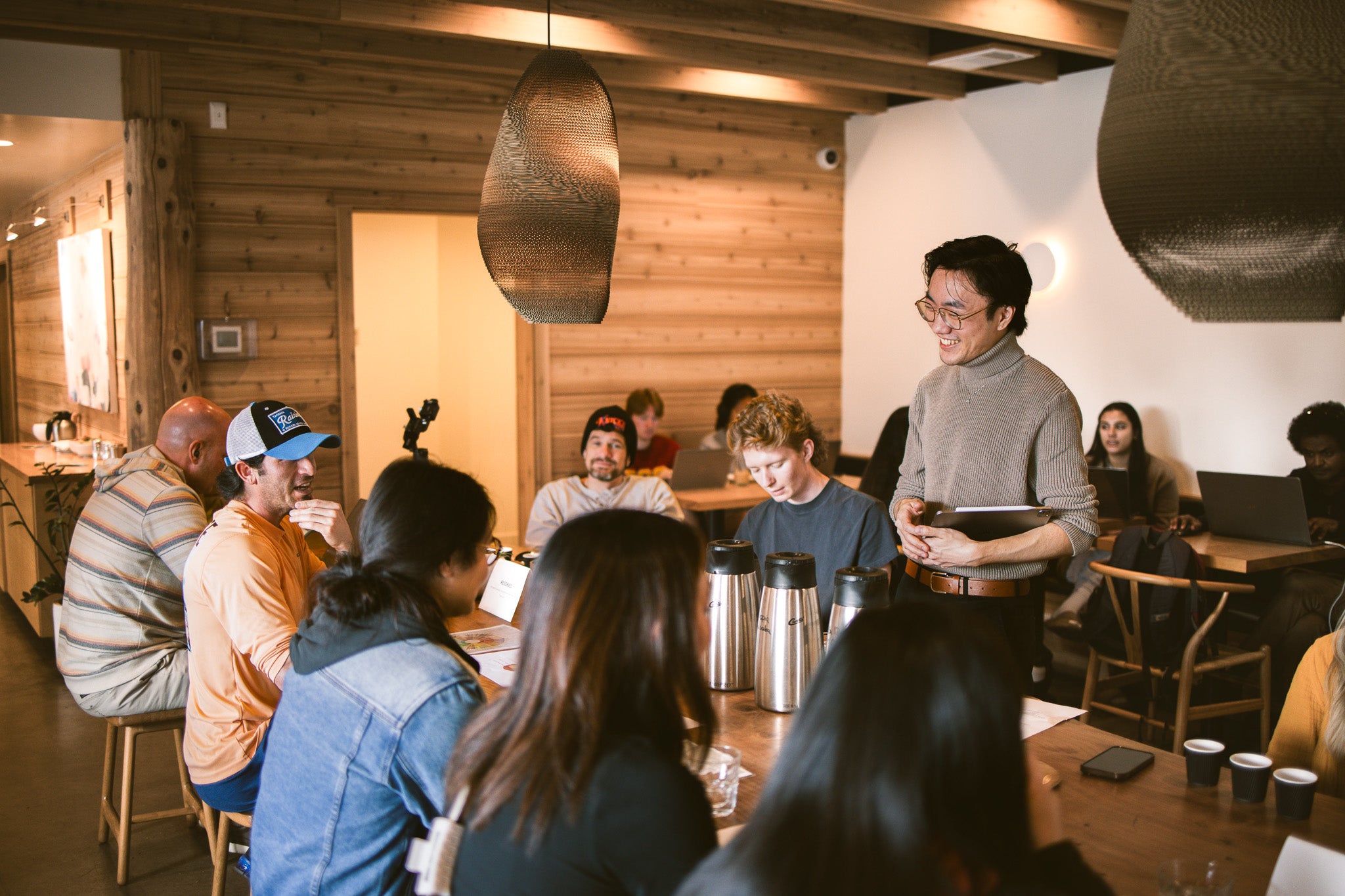 Group of people in a cozy indoor cafe, with wooden walls and pendant lights.