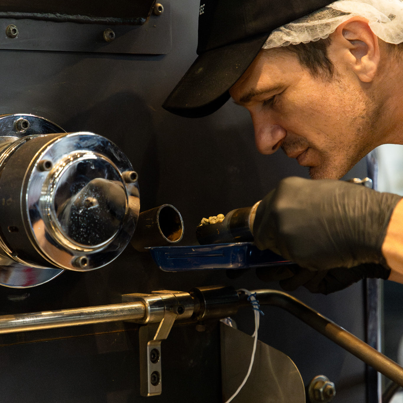 Person working on a coffee roaster with a focus on the machinery.