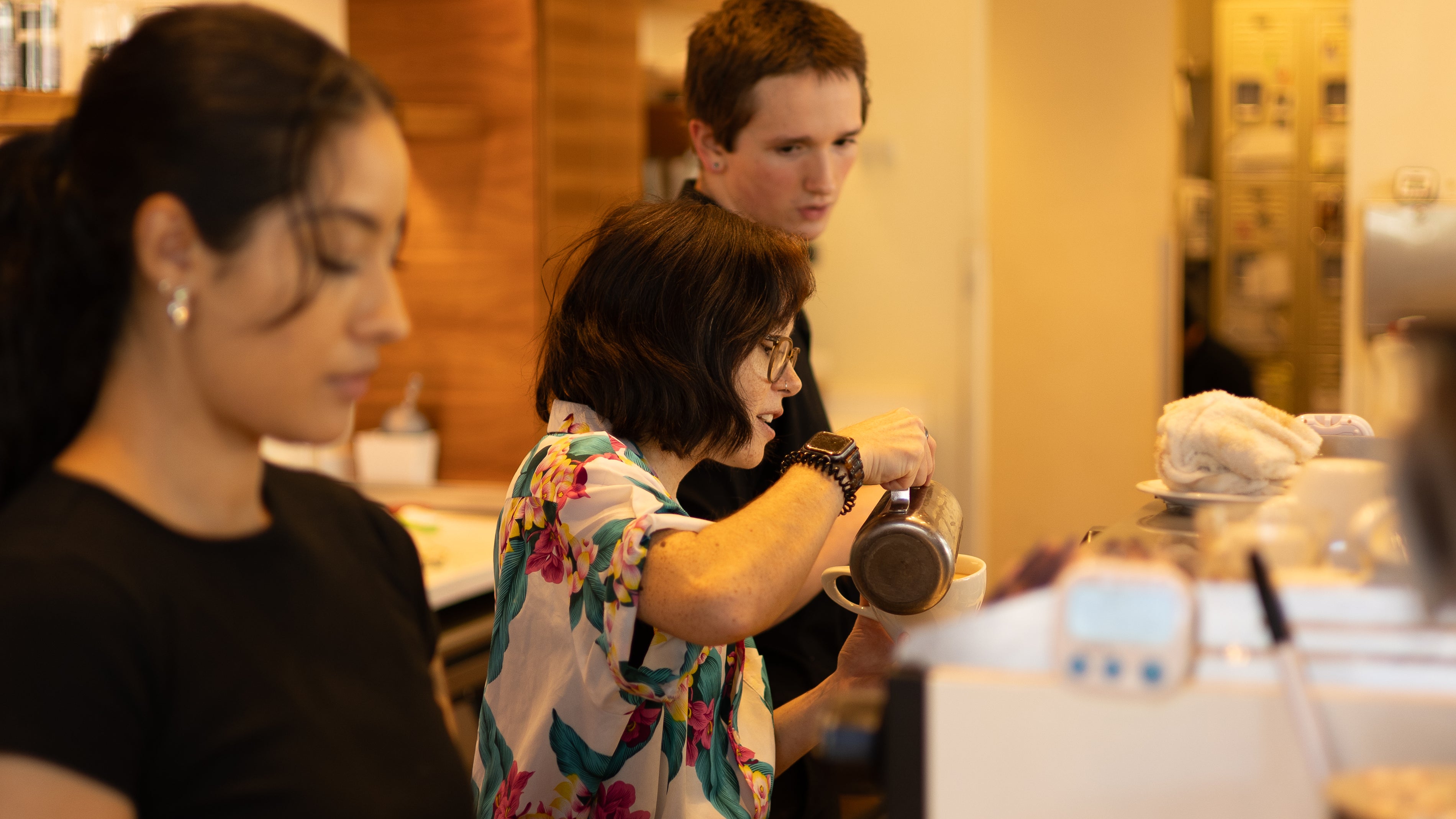 Three people in a cafe setting, with one person using a coffee grinder.