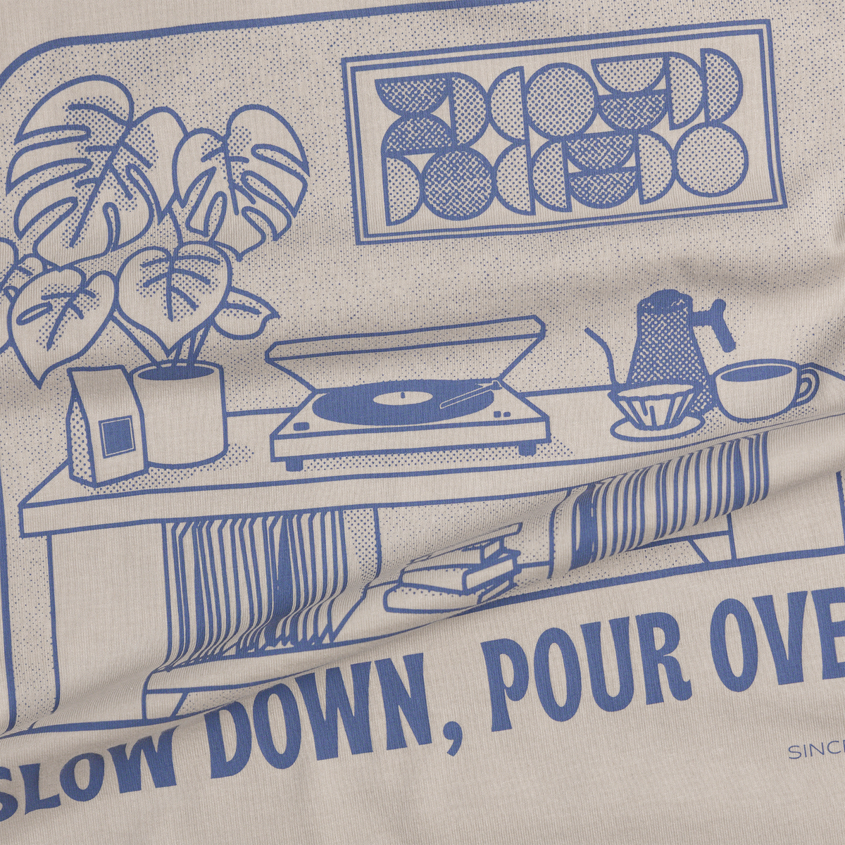 Close-up of a beige fabric product printed with a blue line-art coffee-themed illustration and text reading 'SLOW DOWN, POUR OVER' and 'BLOOMED'.