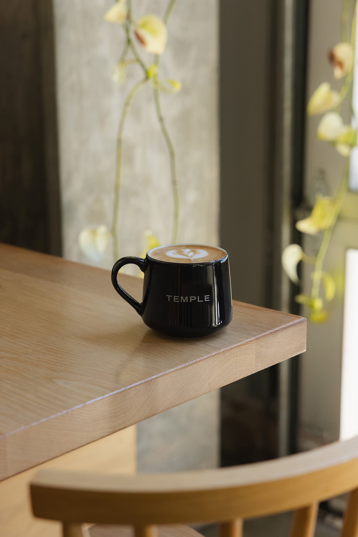 Black mug with 'TEMPLE' branding on a wooden table with flowers in the background