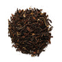 A pile of dry black tea leaves with some lighter, broken pieces visible on a white background.
