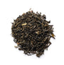 A pile of green tea leaves with visible jasmine blossoms interspersed among them.