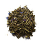 A pile of dried green tea leaves interspersed with small blue flowers.