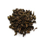A pile of dry, dark oolong tea leaves against a white background.